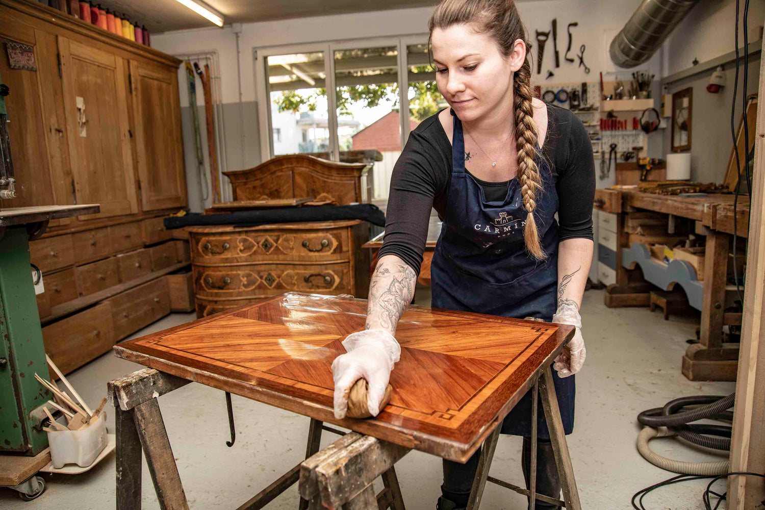 Restauratorin trägt von Hand Öl oder Wachs auf und baut die Oberfläche eines historischen Möbelstücks fachgerecht neu auf in der Werkstatt von Carmine Home in Bern